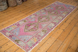 Distressed pink Oushak rug runner corner, showing ivory fringe and faded floral border.