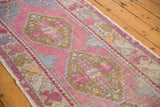 Distressed pink Oushak rug showing geometric florals, colorful border, and original selvage.
