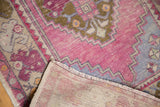 Fringed edge and foundation of a distressed Oushak rug, showing worn pink, blue, bronze pile.