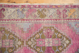 Distressed pink field with bronze geometric patterns and colorful floral border of a vintage Oushak rug.