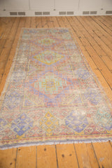 Distressed Oushak runner end displaying geometric hook motifs in unusual mauve, gold, and pale green.