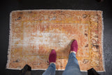 Distressed vintage Oushak rug corner with faded floral motifs and exposed foundation.