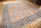 Distressed vintage Oushak rug corner, showing the ornate navy border and soft floral field.