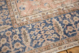 Distressed vintage Oushak carpet corner, featuring worn navy floral border and soft rose field.