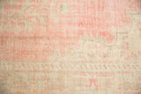 Distressed Oushak carpet detail with faded blush pink floral motifs and mostly even wear on ivory pile.