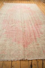 Blush pink and pale beige distressed Oushak rug with secured short fringe showing even wear.
