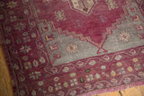 Distressed aubergine and slate stepped patterns on a vintage Turkish Oushak rug corner.