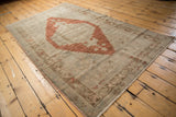 Section of distressed Oushak rug showing faded rust medallion and muted geometric border.