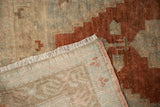 Distressed vintage Oushak rug corner with fringed edge, woven foundation, and chestnut rust geometric pattern.