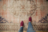 Distressed vintage Oushak rug with exposed knot heads, faded dusty rose and charcoal patterns.