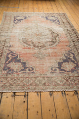 Distressed Oushak rug corner showcasing faded dusty rose field, pale charcoal border, visible knot heads.