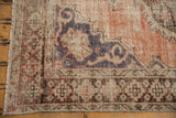 Distressed vintage Oushak rug corner with visible foundation, fringed edge, and patterned border.