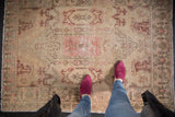Distressed Oushak rug showing low pile, Rococo stylized patterns in faded rose and beige.