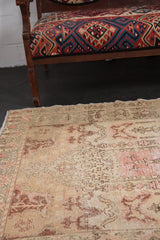 Distressed vintage Oushak rug showing faded patterns and soft ivory, rose hues.