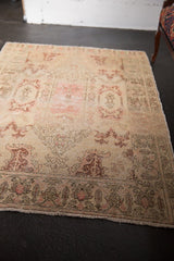 Fringed end of a distressed Oushak rug, with faded ivory, blush patterns and visible wear.