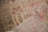 Distressed Oushak rug corner, displaying worn ivory-blush pile, visible foundation, and intact selvage.