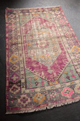 Distressed lower corner of vintage Oushak rug, aubergine, mint geometric motifs, and fringe.