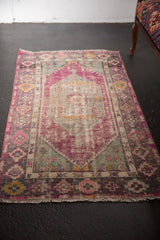 Distressed vintage Oushak rug with oversized diamond medallion in aubergine, mint, grey, and blush.