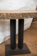 Textured live edge wood tabletop and two straight black iron legs.