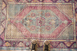 Distressed Oushak rug with faded oversized diamond medallion and worn wine red field.