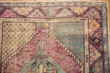 Distressed vintage Oushak rug corner showcasing dusty wine and seafoam green motifs.