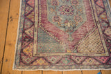 Distressed Oushak rug corner with worn pile, exposed foundation, and blush, sea foam, slate patterns.