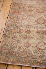 Distressed Sivas rug corner with worn floral motifs in sand, brick red, blush, and slate blue border.