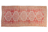 Distressed Oushak runner with repeating serrated medallions in raspberry red and ivory tones.