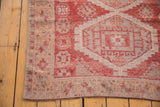 Worn edge of a distressed vintage Oushak runner, with raspberry red and ivory geometric patterns.
