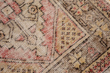 Close-up of distressed Oushak rug pile, showing foundation and faded cherry red, sand tones.
