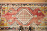 Textured vintage Oushak runner with a diamond medallion, faded red field, and checkered motif.