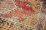 Distressed Oushak rug corner with faded red, saffron yellow, and checkered green patterns, plus fringe.