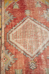 Distressed Oushak rug section: faded tomato red field, diamond medallion with sea foam green checkered motif.