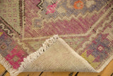 Distressed pink and blue Oushak rug corner, revealing fringe, worn pile, and woven foundation.