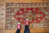 Distressed Oushak rug corner with low pile texture, cherry red field, and colorful floral border.