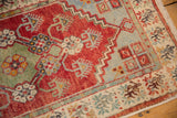 Distressed vintage Oushak rug displaying low pile texture and cherry red floral elements.