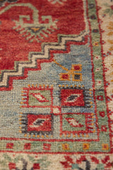 Textured low pile vintage Oushak rug showing red, blue, and green geometric distressed motifs.