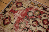 Distressed Oushak rug corner showing cherry red, beige floral pattern, and meandering border with wear.