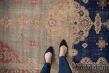 Distressed Sivas rug with abrashed blush field, navy floral medallion, and foundation showing.