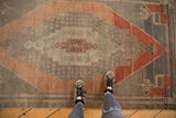 Distressed Oushak runner detail featuring germinating plants and pinwheel florals in blush rust and silver.