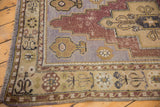 Vintage distressed Oushak rug corner with visible wear, pale lavender field, and ornate floral border.