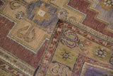 Distressed vintage Oushak rug corner with fringe, showing worn pile and intricate border.