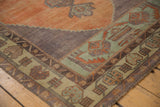 Distressed vintage Oushak rug corner with pale green geometric border and rust orange field.