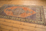 Distressed Oushak rug corner, showcasing faded geometric border details in orange and oxidized green.
