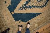 Distressed vintage Oushak rug corner, showing navy blue stepped geometric spandrel and beige field.