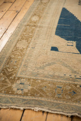 Distressed Oushak carpet corner with even wear, pale bronze border, and navy motifs.