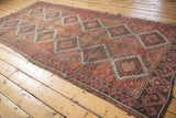 Distressed Oushak rug texture showing repeating diamond medallions in faded cherry red, charcoal, and ivory.
