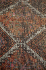 Distressed Oushak rug pile featuring faded rust, charcoal, and ivory diamond motifs.