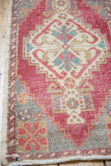 Distressed Oushak rug corner, revealing worn cherry red pile, ivory pattern, and fringe.