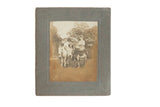 Antique sepia photograph of two women riding donkeys, mounted on a grey paperboard frame.